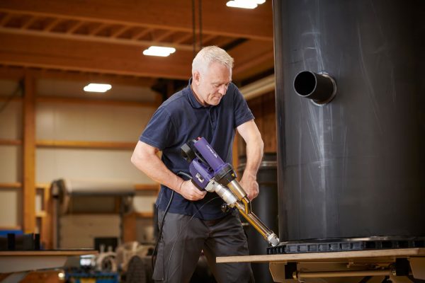 Técnico utilizando a extrusora manual Weldy Booster EX3 para soldar reservatório plástico em ambiente industrial.