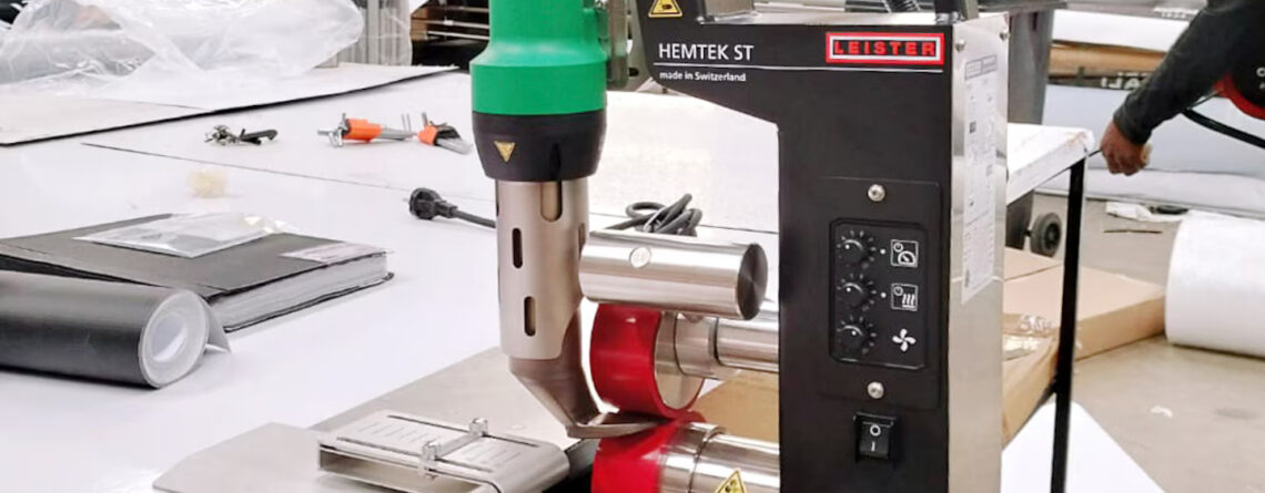 Máquina de soldagem Leister HEMTEK ST em bancada de produção, aplicada no fechamento de bainhas para sinalização