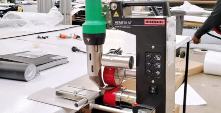 Máquina de soldagem Leister HEMTEK ST em bancada de produção, aplicada no fechamento de bainhas para sinalização