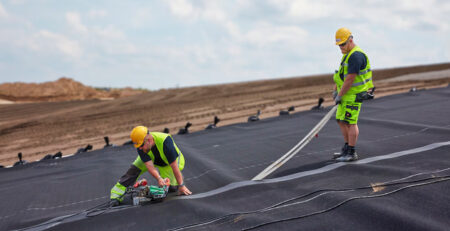 Equipe da Solmax realizando soldagem de geomembrana para impermeabilização de área industrial, usando máquina automática Leister em campo