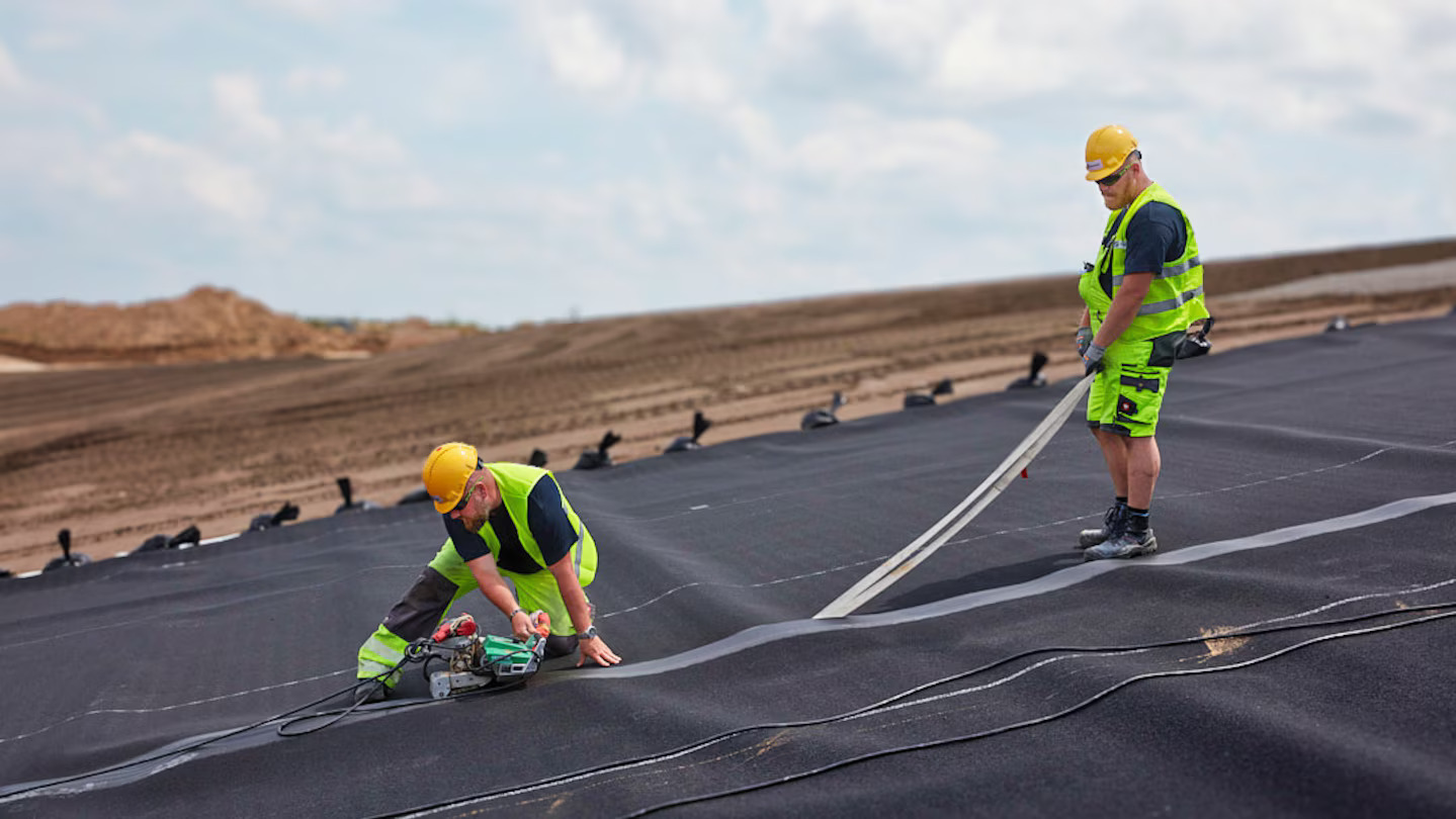 Equipe da Solmax realizando soldagem de geomembrana para impermeabilização de área industrial, usando máquina automática Leister em campo