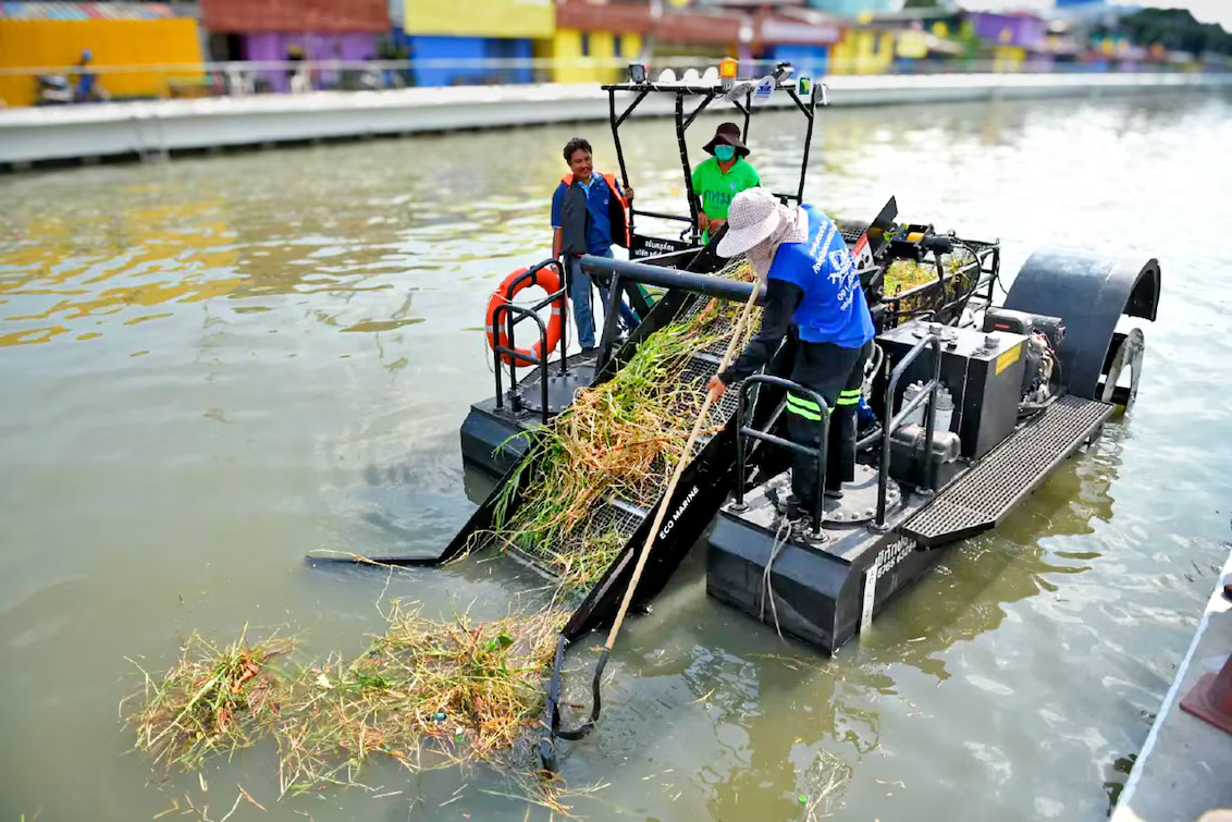 Embarcação de coleta de resíduos em PEAD navegando em canal urbano, equipada com sistema de esteira para remoção de lixo, construída com soldagem por extrusão Leister