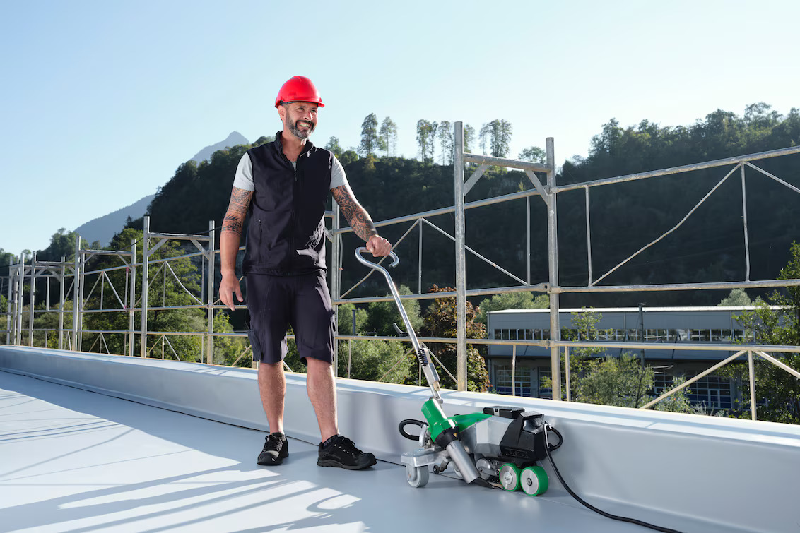 Técnico utilizando a soldadora automática Leister VARIMAT 500 para soldagem de membrana em cobertura plana, garantindo velocidade, precisão e qualidade em aplicações de impermeabilização